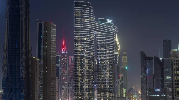 ドバイのダウンタウンや金融街の窓に明かりが灯る未来的なタワーや照明付き高層ビル 都市のスカイライン航空夜のタイムラプス 暗い空 — ストック写真