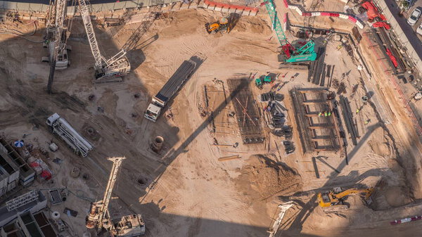 Heavy machinery for earthmoving with crane, truck and bulldozer. Aerial view construction site with a foundation pit of new skyscraper timelapse. Earthwork in excavation and backfilling of soil.