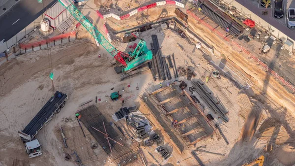 新しい高層ビルのタイムラプスの基礎ピットと空中ビュー建設現場 掘削や土壌のバックフィリングでの土仕事 クレーン荷役トラックでの移動のための重機 — ストック写真