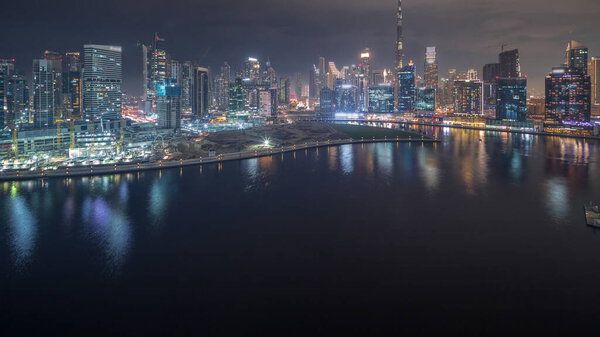 Aerial view to Dubai Business Bay and Downtown with the various skyscrapers and towers along waterfront on canal night timelapse. Large construction site with cranes