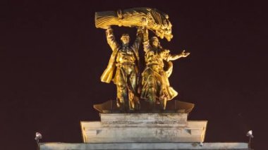 Sculpture Tractor operator and collective farmer on the top of entrance to All-Russia Exhibition Centre timelapse hyperlapse. Moscow, Russia. Orange illumination at night
