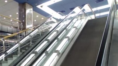 Trenlerin zaman ayarlı olduğu modern bir metro istasyonu. Yürüyen merdivenlerde insanlar girip çıkıyor.