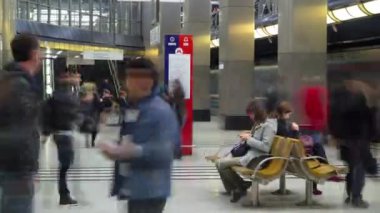 Trenlerin zaman ayarlı olduğu modern bir metro istasyonu. İnsanlar bir bankta oturup bekliyorlar. Metro haritası tezgahta