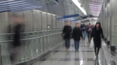 Nakil koridoru zaman ayarlı modern bir metro istasyonu. İstasyonlar arasında yürüyen insanlar. Yerde yansımalar var.