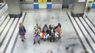 Trenlerin zaman ayarlı olduğu modern bir metro istasyonu. Platformun ortasındaki bankta bekleyen insanlara tepeden bakıyorum.