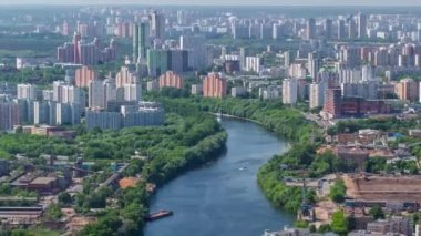 Moskova şehrinin gökdelenlerinden panoramik hava görüntüsü. Nehirde yüzen tekneler ve arkasında yeşil ağaçlar olan birçok konut binası.