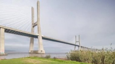 Architectural landmark Vasco da Gama Bridge over the Tagus River in Lisbon, Portugal. Green grass and cloudy sky. The longest bridge in the European Union.