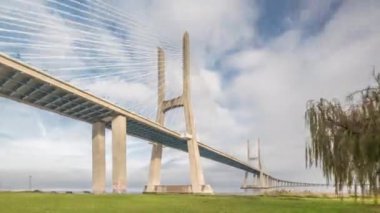 Architectural landmark Vasco da Gama Bridge over the Tagus River in Lisbon, Portugal. Green lawn with trees and cloudy sky. The longest bridge in the European Union.