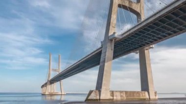 Vasco da Gama bridge timelapse hyperlapse with reflection on water and blue cloudy sky. Cable-stayed bridge and Tagus river. Lisbon, Portugal.