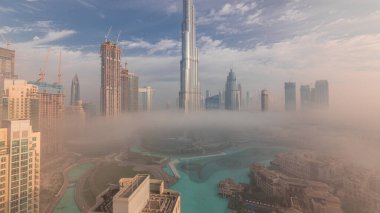 Sabahın erken saatlerinde sis sırasında Dubai şehrinin havadan panoramik görüntüsü. Gökdelenler ve gökdelenlerle dolu fütüristik şehir siluetinde gün doğumu. Güneş cam yüzeyden yansıyor