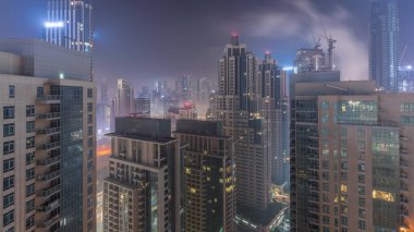 Dubai gökdelenleri tüm gece boyunca business bay bölgesinde aydınlık. Birleşik Arap Emirlikleri 'nde şehir merkezindeki kulelerin tepesinden sisli hava manzarası. Işıklar kapanıyor.