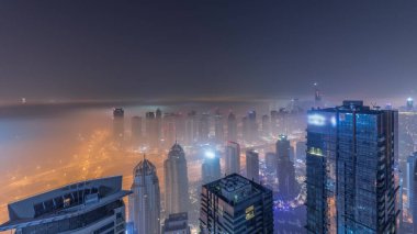 Dubai Marina Panorama 'sı JLT gökdelenleri ve golf sahası ile tüm gece boyunca, Dubai, Birleşik Arap Emirlikleri. Sisi olan kulelerin üzerinden hava görüntüsü. Işıklar sönerken şehrin ufuk çizgisi