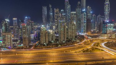 Dubai Marina 'nın gökdelenleri, gün batımından sonra gün batımından sonra karayolu trafiğiyle aydınlık konutlu binalar. JLT bölgesinden hava üst görünümü