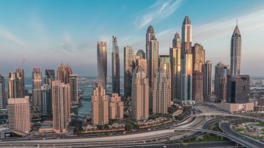 Dubai Marina karayolu kavşağı spagetti kavşağı gece gündüz geçiş. Arka planda en uzun gökdelenler aydınlatılıyor. Güneş doğmadan önce JLT bölgesinden hava üst görünümü