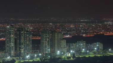 Moon rising over greens and al barsha heights district area night from Dubai marina. Towers and skyscrapers with traffic on roads from above