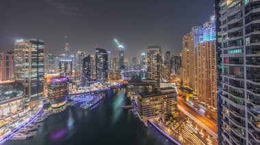 Kanal çevresindeki Dubai marina gökdelenlerinin hava panoramik görüntüsü ve gece gündüz yüzen tekneler. Günbatımından sonra beyaz tekneler yat kulübüne park edilir.