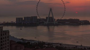 Bluewater adasında günbatımı modern mimari ve dönme dolap anteniyle. Dubai marinası ve JBR yakınlarındaki yeni boş zaman ve yerleşim alanı. Turuncu gökyüzü