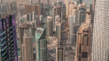 Dubai Marina 'nın gökdelenlerle çevrili yapay bir kanalı sabah güneş doğarken kıyı şeridi boyunca uzanan gökdelenleri gösteren panoramik görüntüsü. Yüzen yatlar ve tekneler. Dubai, BAE