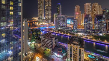 Günbatımından sonra Dubai Marina gökdelenleri ve JBR bölgesi aydınlık lüks binalar ve gece geçişleriyle dolu tatil beldeleri. Palmiyeler ve kanalda yüzen teknelerle dolu bir liman.