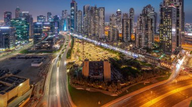 Business Bay hava sahasında modern kuleleri olan Bay Bulvarı 'ndaki panoramik havadan geceye geçiş, Dubai, BAE. Büyük otoparkın yakınındaki yolda trafiği olan gökdelenler.