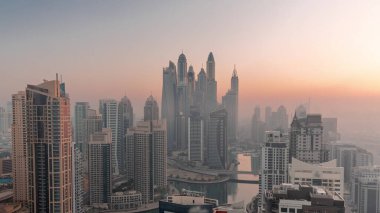 View of various skyscrapers in tallest recidential block in Dubai Marina aerial night to day transition with artificial canal. Many towers and yachts foggy morning before sunrise