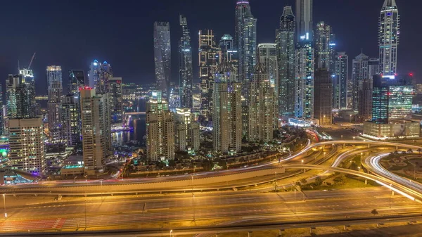 Skyscrapers of Dubai Marina with illuminated highest residential buildings day to night transition after sunset with traffic on a highway. Aerial top view from JLT district