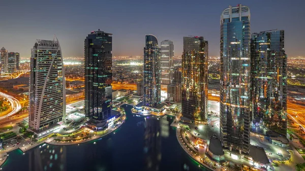 Tall residential buildings at JLT district aerial day to night transition panoramic, part of the Dubai multi commodities centre mixed-use district. Villa houses on a background