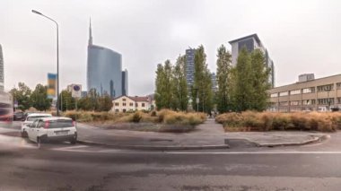 Panorama showing skyscrapers and towers from park with outumn treea and green lawn timelapse. Located between Piazza Gae Aulenti and the Isola district. Traffic on a road. Milan. Italy
