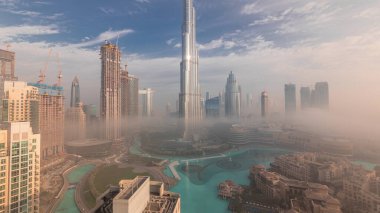 Sabahın erken saatlerinde sis sırasında Dubai şehrinin havadan panoramik görüntüsü. Gökdelenler ve gökdelenlerle dolu fütüristik şehir siluetinde gün doğumu. Güneş cam yüzeyden yansıyor