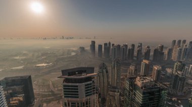 Dubai Marina Panoraması, güneş doğarken JLT gökdelenleri ve golf sahası, Dubai, Birleşik Arap Emirlikleri. Yukarıdan hava manzarası sisli bir sabah. Turuncu gökyüzü ile şehir silueti
