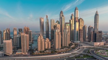 Dubai Marina karayolu kavşağı spagetti kavşağı gece gündüz geçiş. Arka planda en uzun gökdelenler aydınlatılıyor. Güneş doğmadan önce JLT bölgesinden hava üst görünümü