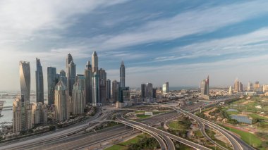 Dubai Marina karayolu kavşağındaki panorama spagetti kavşağı bütün gün sürdü. Arka planda hızla hareket eden gölgeli en uzun gökdelenler. JLT bölgesinden hava görüntüsü. Bulutlu gökyüzü