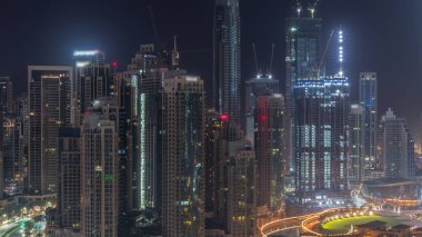 Futuristic aerial cityscape during all night with illuminated architecture of Dubai downtown with lights turning off. Many tall skyscrapers and towers. New construction site. United Arab Emirates.