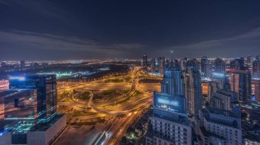 JLT ve Dubai Marina arasındaki büyük otoyol kavşağı gece boyunca Şeyh Zayed Yolu hava sahasında kesişmiş. Kulelerin ve gökdelenlerin yakınındaki golf sahasında ışıklar sönüyor.