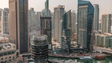 Arka planda JLT gökdelenleri olan Dubai Marina Skyline. Güneş doğarken cam yüzeyi ve yatları olan kuleler.