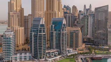 Dubai Marina gökdelenleri ve JBR bölgesi güneş doğarken lüks binalar ve tatil köyleri. Palmiyeleri ve yeşil çimenleri olan limana.