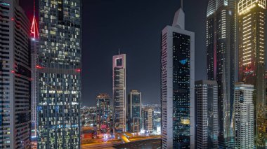 Panorama, Dubai Uluslararası Finans Bölgesi 'nin gökdelenlerle aydınlatılmış birçok gecesini gösteriyor. Çok katlı otoparkların yakınındaki bir yolda trafik vardı. Dubai, BAE.