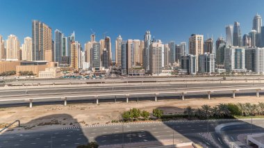 Panorama, Dubai Marina gökdelenlerini ve Şeyh Zayed yolunu metro antenli gösteriyor. Modern kulelerin yakınındaki bir otoyolda trafik var, Birleşik Arap Emirlikleri