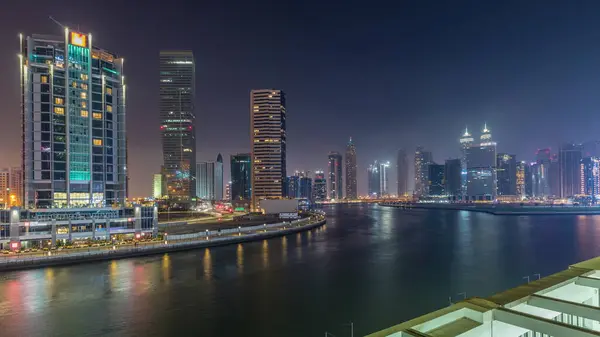 Modern city architecture in Business bay district at sunset. Panoramic aerial view of Dubai\'s skyscrapers reflected in water day to night transition