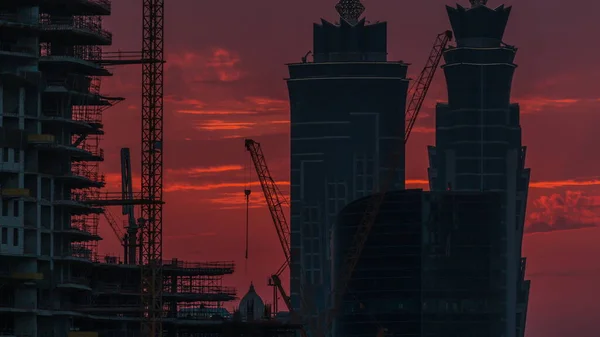 日没の空中にあるドバイのビジネスベイタワーに近いビュー いくつかの高層ビルと建設中の新しいタワーのルーフトップビュー オレンジの空と建物のシルエット — ストック写真