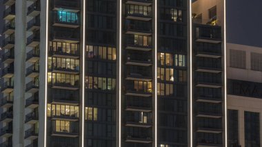 Şehrin hava zaman ayarlı yerleşim bölgesinde parlayan pencereleri olan uzun apartmanlar. Kulelerin ve gökdelenlerin tepesindeki odalarda akşam ışığı