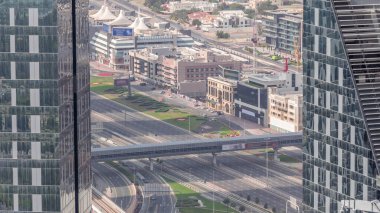 Gökyüzünden Dubai şehir merkezindeki işlek yol kavşağına kadar hava görüntüsü. Şeyh zayed yolunda her iki yöne giden renkli arabalar ve kamyonlar. Gökdelenlerin uzun gölgeleri