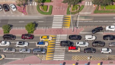 Yukarıdan, Dubai zaman diliminde zebrayla dolu yoğun bir yol trafiğine doğru hava görüntüsü. Arabalar iki yönde de dümdüz gidiyor ve yayalar yoldan geçiyor. Otoparkı olan finans bölgesi