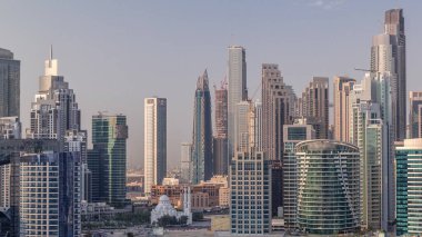 Dubai İşletme Koyu 'nun gökdelenleri ve su kanallarının zaman çizelgesi olan şehir manzarası. Rıhtımda konut ve ofis kuleleri olan modern gökyüzü. Yüksek binalarla çevrili bir cami.