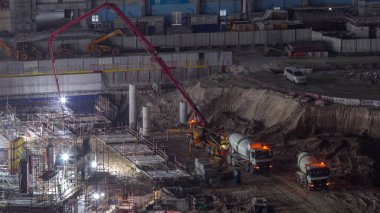 Apartman kompleksinin inşaatı için temel çukurunda yığınlar var. Somut karıştırıcı ve pompa olarak ağır makinelerle derin tesis ve kazı, Dubai 'de buldozerler