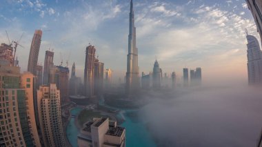Sabahın erken saatlerinde, sis gecesinden gündüze geçiş zamanlarında Dubai şehrinin hava görüntüsü. Gökdelenleri ve kuleleri olan gelecekçi şehir gökdelenleri ve gökdelenleri yukarıdan gün doğumunda
