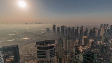 Dubai Marina Panoraması 'nda güneş doğarken JLT gökdelenleri ve golf sahası, Dubai, Birleşik Arap Emirlikleri. Yukarıdan hava manzarası sisli bir sabah. Turuncu gökyüzü ile şehir silueti