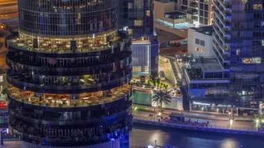 Dubai marinası rıhtımı ve her katta farklı restoranlar bulunan bir bina tüm gece boyunca. Rıhtımı olan yatlar ve ışıkları sönen gökdelenler.