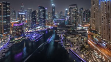 Panorama Dubai marinasının hava manzarasını gösteriyor. Kanal etrafındaki gökdelenleri aydınlatıyor. Yüzen yatlar ve gece saatleri var. Jlt ve JBR bölgelerindeki kuleler. Yat kulübünde beyaz tekneler var.
