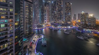 Panorama, Dubai marinasında gece hava sahasında lüks yat hangarını gösteriyor. Rıhtım boyunca modern gökdelenler ve limanda yüzen tekneler.